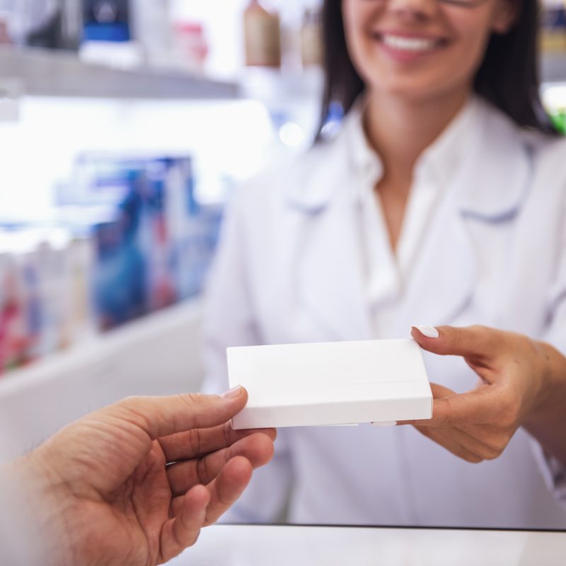 Farmacéutica entregando un medicamento a un cliente.